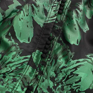 Detailed macro view of green floral jacquard fabric with delicate black buttons on a dress.
