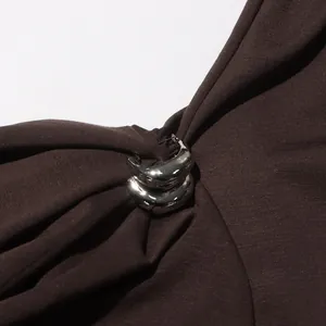Detalle de un anillo plateado que recoge la tela marrón plisada de este vestido retro.
