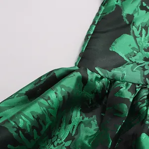 Close-up detail of emerald green floral jacquard fabric with elegant pleated textures.