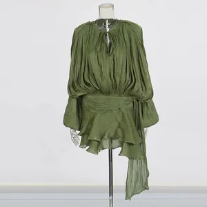 Full view of pleated green dress on a clear mannequin against a white studio background