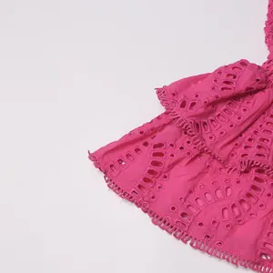 Detailopname van felroze geborduurde stof met delicate ruches en oogjesdetails voor een jurk