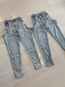Detail of light blue denim pants with irregular cut-outs and zipper accents.
