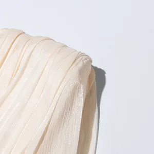 Macro view showing the elegant pleated fabric texture of a cream designer mini dress