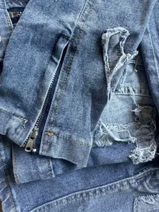 Close-up of blue denim jacket showing metal zipper and distressed ripped details.
