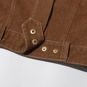 Dettaglio di giacca marrone vintage con bottoni a pressione dorati e trama twill
