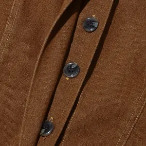 Dettaglio di bottoni in marmo scuro e trama twill su giacca vintage marrone lavata.