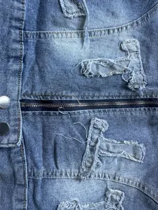 Close-up detail of distressed blue denim jacket featuring a zipper and ripped texture