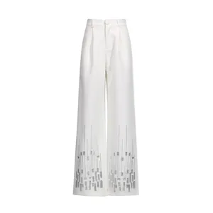 Detail of white high-waisted straight trousers with sequin geometric patterns at hem.