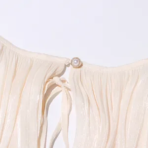Detail shot of pearl button and textured pleated fabric on elegant cream dress