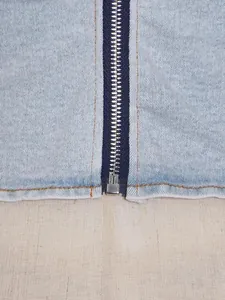 Close-up detail of a silver metal zipper and stitching on light blue wash denim garment