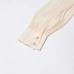 Close-up of elegant pleated sleeve cuff featuring decorative pearl buttons on a cream dress