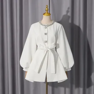 Close-up view of elegant white jacket with rhinestone collar on a gold mannequin