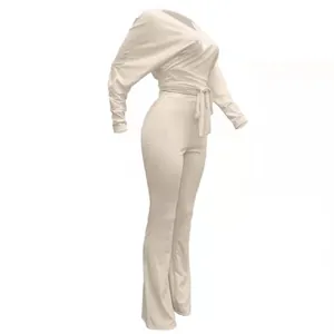Dettaglio della tuta a coste color crema con cintura a fiocco e drappeggio elegante.