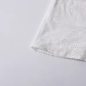 Macro detail of intricate floral eyelet embroidery and scalloped hem on white lace fabric.