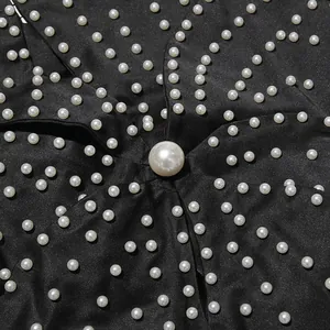 Close-up detail of white pearl beading on black satin fabric top.
