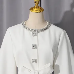 Close-up of elegant white jacket with rhinestone collar and square gem buttons
