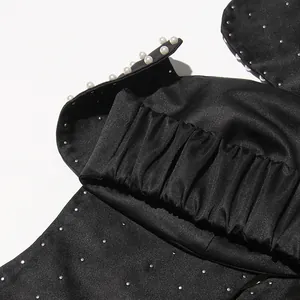 Detail view of a black satin tube top featuring elegant pearl trim and silver stud accents.