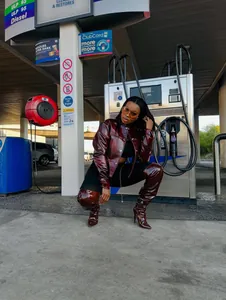 Fashionable short wine red shiny leather jacket for women shown in urban gas station
