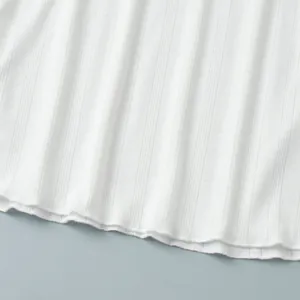 Close-up of white ribbed knit fabric with delicate heart pointelle pattern and lettuce hem