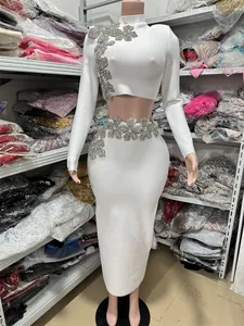 Detail view of white long-sleeved bandage crop top and skirt with rhinestone floral decorations.