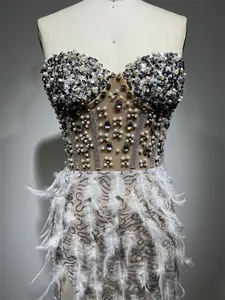 Dettaglio di un elegante abito da sera con strass di lusso e delicate piume bianche.