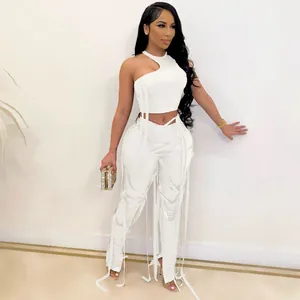 Completo sexy bianco a due pezzi con top asimmetrico e pantaloni con ritagli e lacci.