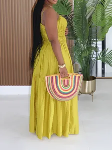 Side view of a yellow boho sleeveless tiered maxi dress styled with a colorful woven bag