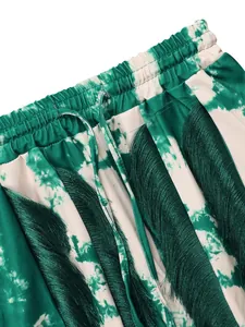 Detail view of green tie-dye pants featuring tassel fringe and drawstring waist.