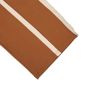 Close-up detail of cotton sweatpants with a stylish cream side stripe in rust brown