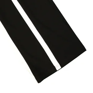 Macro detail view of black athletic pants with white side stripes and stitched hem.