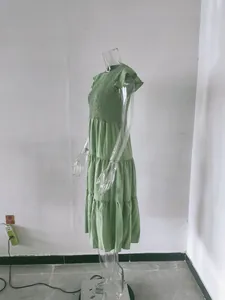 Side view detail of a green smocked tiered dress with flutter sleeves on a clear mannequin.