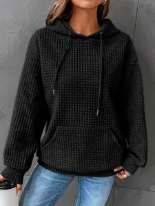 Close-up of black waffle knit hoodie featuring hood drawstring and kangaroo pocket