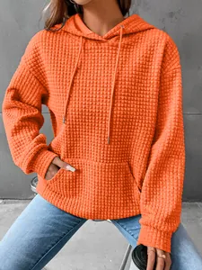 Detailed view of bright orange waffle knit hoodie featuring a kangaroo pocket and drawstring hood