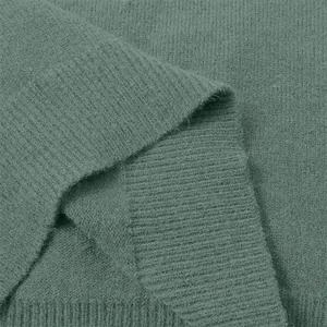 Close-up macro view of the soft green knit sweater fabric texture showing ribbed hem detail