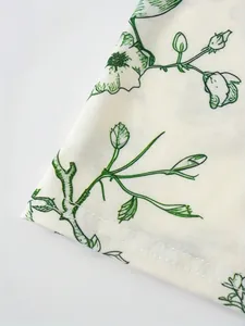 Makrodetail aus weißem Stoff mit grünem Blumenmuster und feiner Saumnaht.