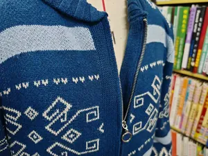Close-up detail of blue men's knitted cardigan with white geometric pattern and ring zipper