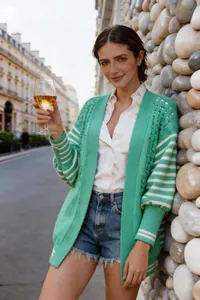Modella indossa un cardigan in maglia traforata verde con maniche a righe bianche all'aperto