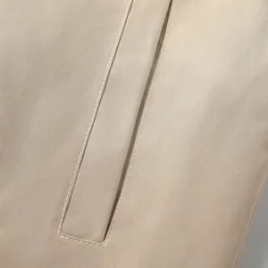 Detailed close-up of beige windproof jacket fabric with precise white stitching detail