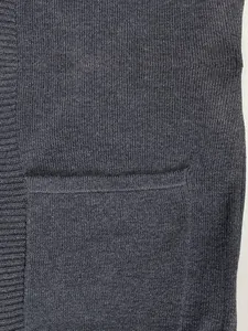 Detailopname van een gebreid damesvest met functionele zak en geribbelde randtextuur.