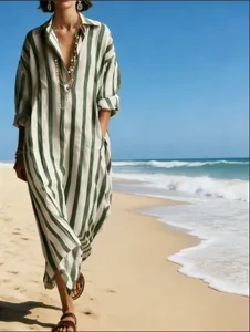 Detail view of a loose green and white striped V-neck maxi dress on a sunny beach.