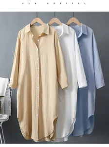 Détail de robes chemises longues en lin amples en kaki, blanc et bleu sur des cintres.