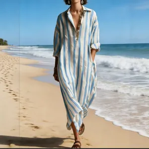 Elegant loose blue and white striped V-neck maxi dress with pockets walking on a sunny beach