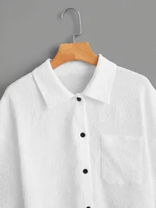 Detailed view of a white textured crinkle fabric shirt with black buttons and a front pocket