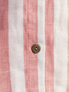 Gros plan sur le tissu d'une chemise rayée rose et blanc avec bouton en bois