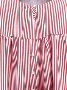 Détail en gros plan des boutons et de la couture à volants sur une blouse rayée rouge.