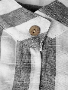 Détail d'une chemise en lin à rayures grises montrant le col et un bouton en bois.