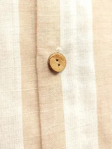Gros plan d'un bouton en bois naturel sur le tissu rayé beige et blanc d'une chemise casual.
