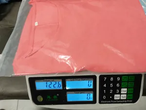Detail view of a pink cotton linen blouse being weighed on a digital scale showing 123g.
