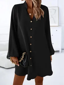 Detail view of a black long-sleeved A-line dress with V-neck and button closure.