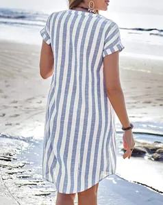 Back view of a breezy blue and white vertical striped summer shirt dress on a beach.
